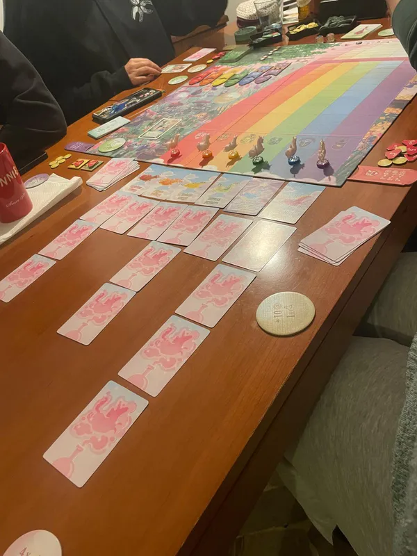 A rainbow-themed board game with rows of pink cards laid out on a wooden table