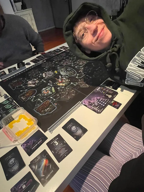 Peeking out of a green hoodie beside a sci-fi board game in progress