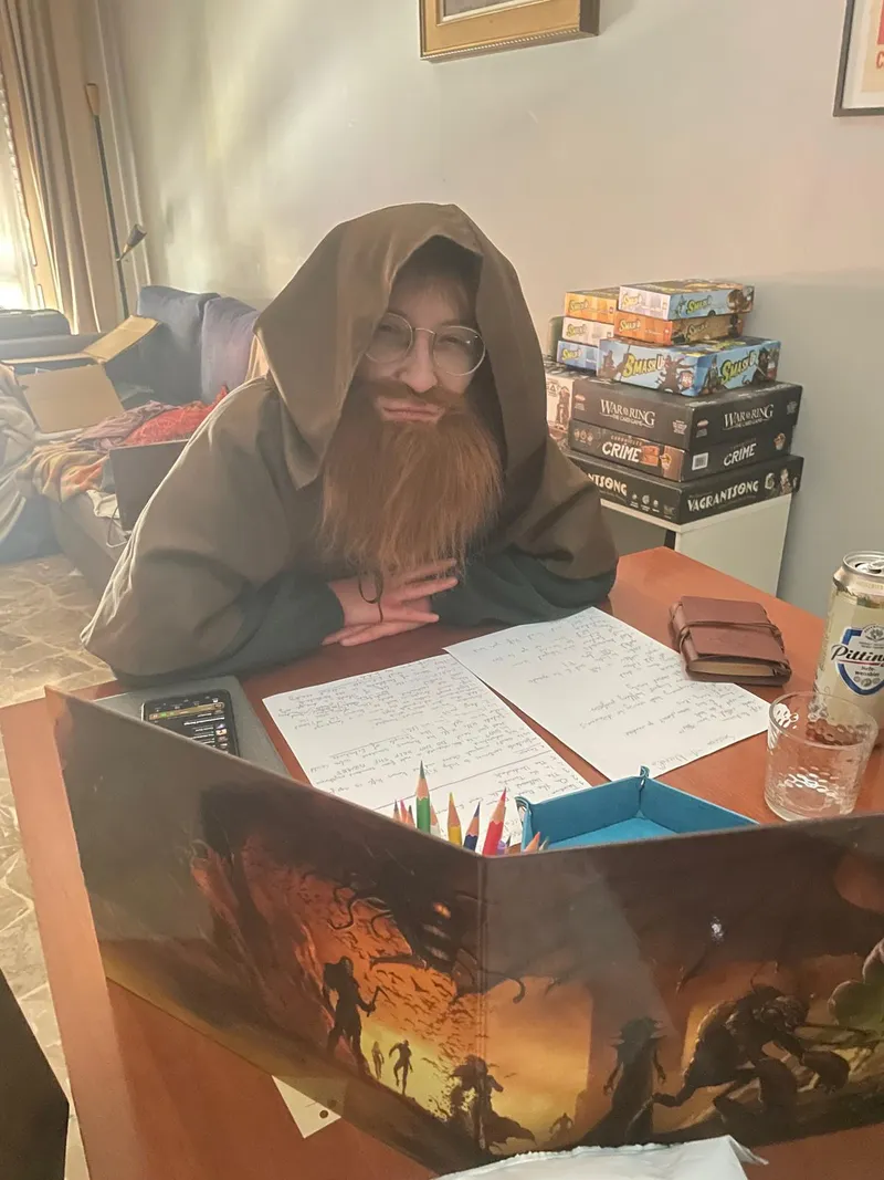 Noé dressed as a hooded, bearded game master, sitting behind a DM screen with handwritten notes